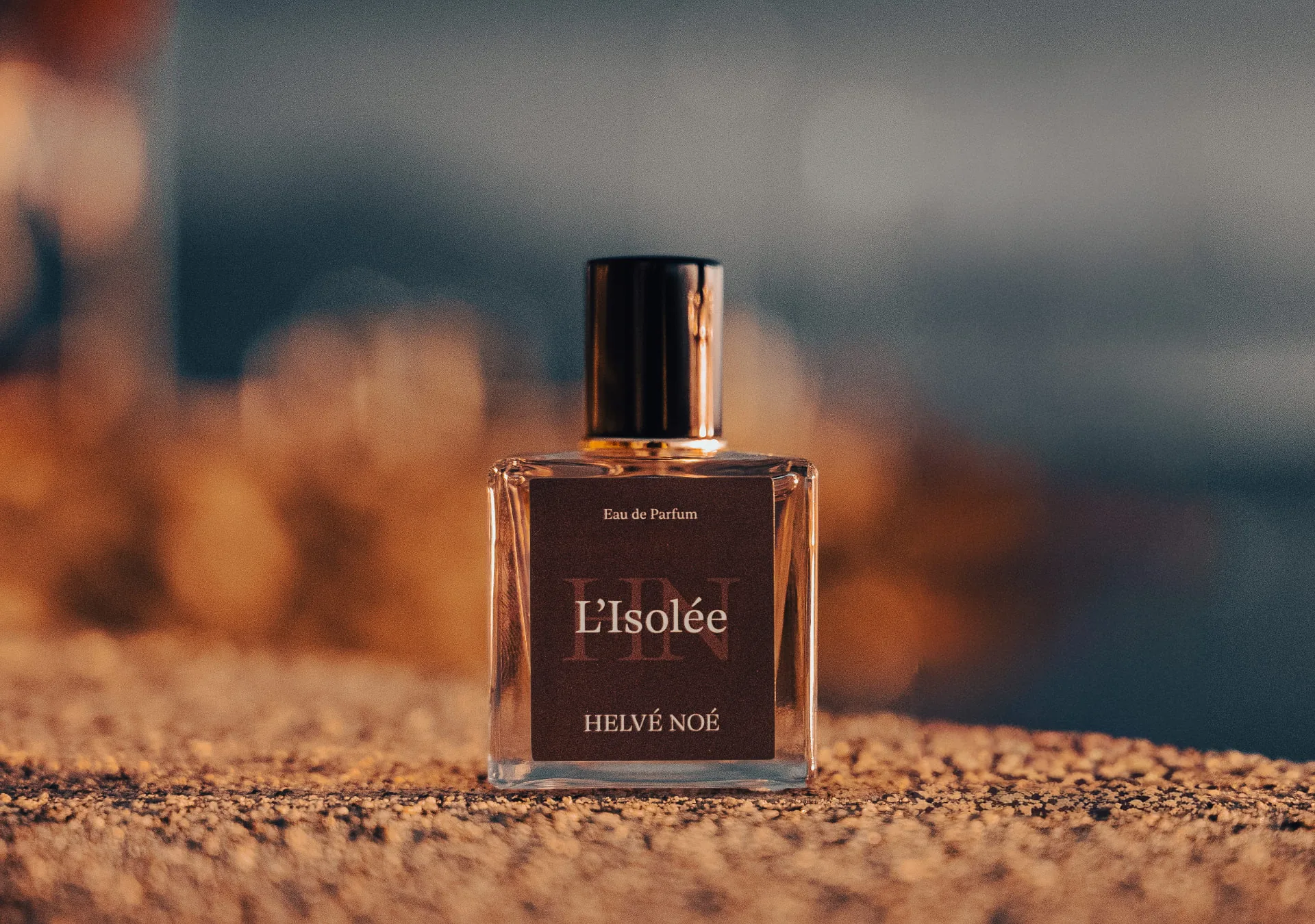 Flakon L’Isolée von Helvé Noé auf Sand im Sonnenuntergang